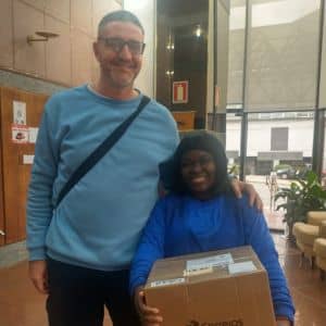 Professor do Instituto Alce doa computador a aluna refugiada haitiana, simbolizando inclusão digital e apoio à escolaridade na adultez.