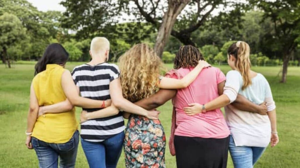 Quatro mulheres abraçadas de costas em parque, simbolizando união e empoderamento feminino no grupo de Terapia Comunitária.